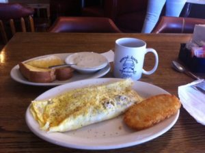 A plated omelette and hash-brown with a side of Texas toast and gravy and a cup of North South coffee